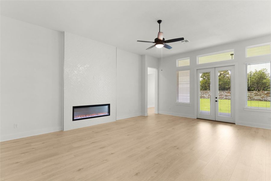 Unfurnished living room featuring wood finished floors, ceiling fan, a large fireplace, and french doors Unfurnished living room featuring wood finished floors, ceiling fan, a large fireplace, and french doors