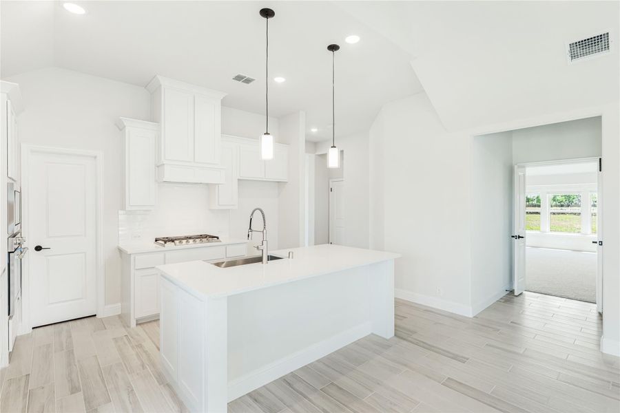 White kitchen with large island, pendant lights, white cabinets, and light wood-look tile floors