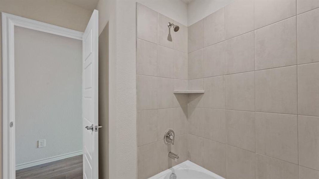 Tub and shower combination featuring extensive light-toned tile work, a built-in corner shelf, and chrome fixtures Tub and shower combination featuring extensive light-toned tile work, a built-in corner shelf, and chrome fixtures