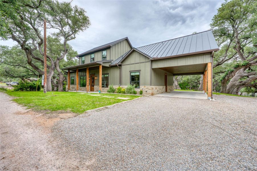 Modern farmhouse exterior featuring vertical siding, a metal roof, stone accents, a covered front porch with wood columns, and a gravel driveway