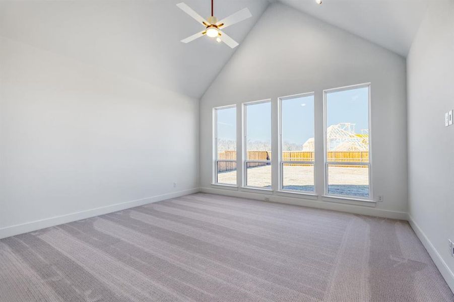 Spare room featuring light colored carpet, a ceiling fan, and a high ceiling