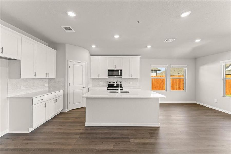 Kitchen with dark wood-type flooring, sink, an island with sink, white cabinetry, and appliances with stainless steel finishes