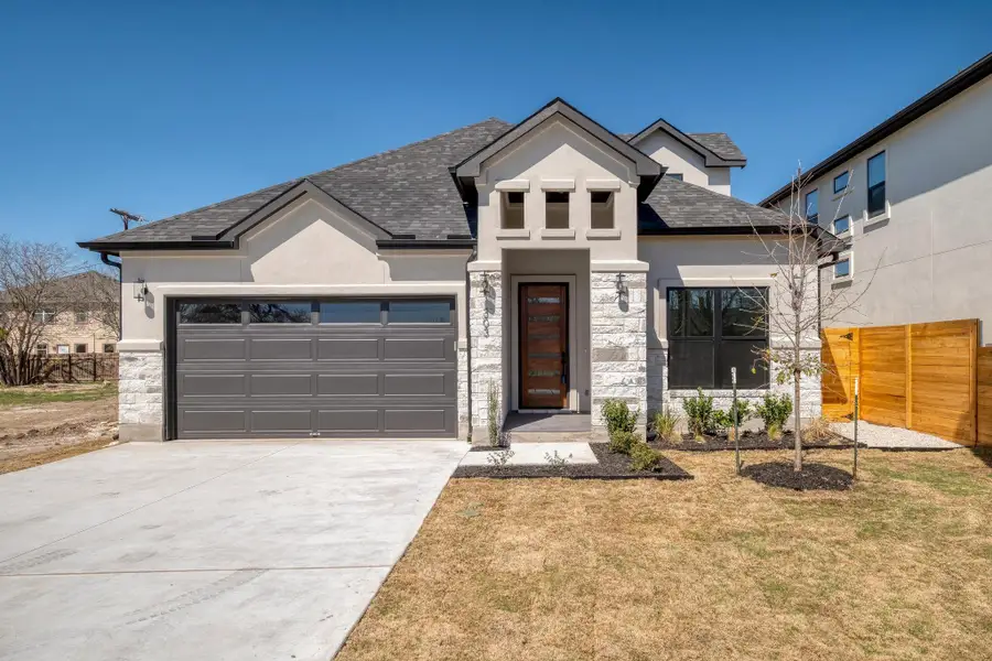 View of front of home featuring a garage, stone siding, fence, and stucco siding