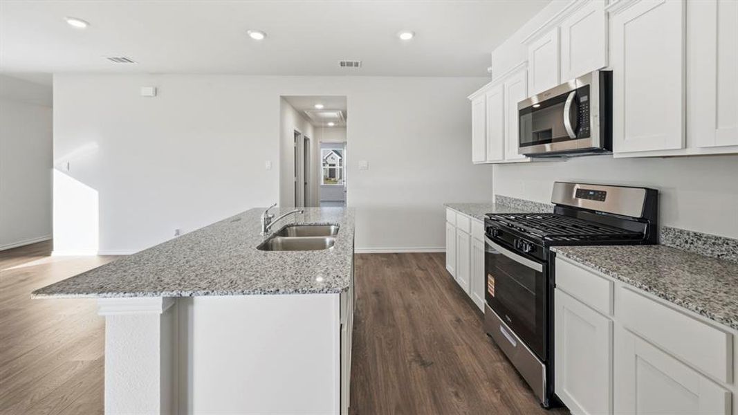 Kitchen featuring stainless steel appliances, light stone counters, white cabinetry, an island with sink, and recessed lighting Kitchen featuring stainless steel appliances, light stone counters, white cabinetry, an island with sink, and recessed lighting