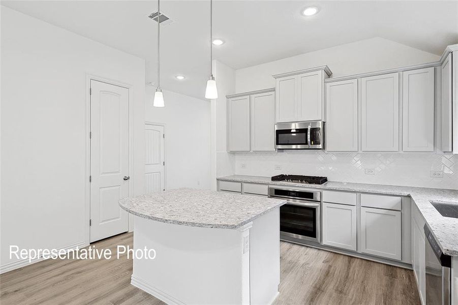 Modern kitchen featuring light cabinetry, stainless steel appliances, a center island with pendant lighting, and wood-finish flooring