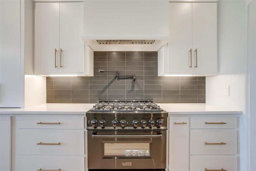 Kitchen with luxury range, white cabinets, and tasteful backsplash