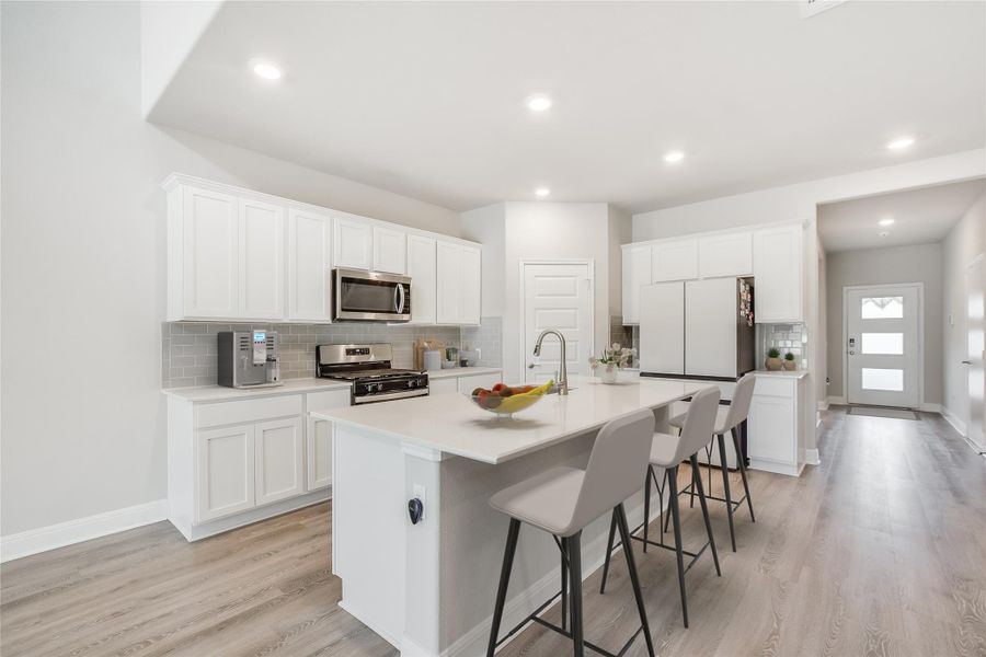 Kitchen featuring white cabinets, appliances with stainless steel finishes, a breakfast bar area, a kitchen island with sink, and light wood-type flooring