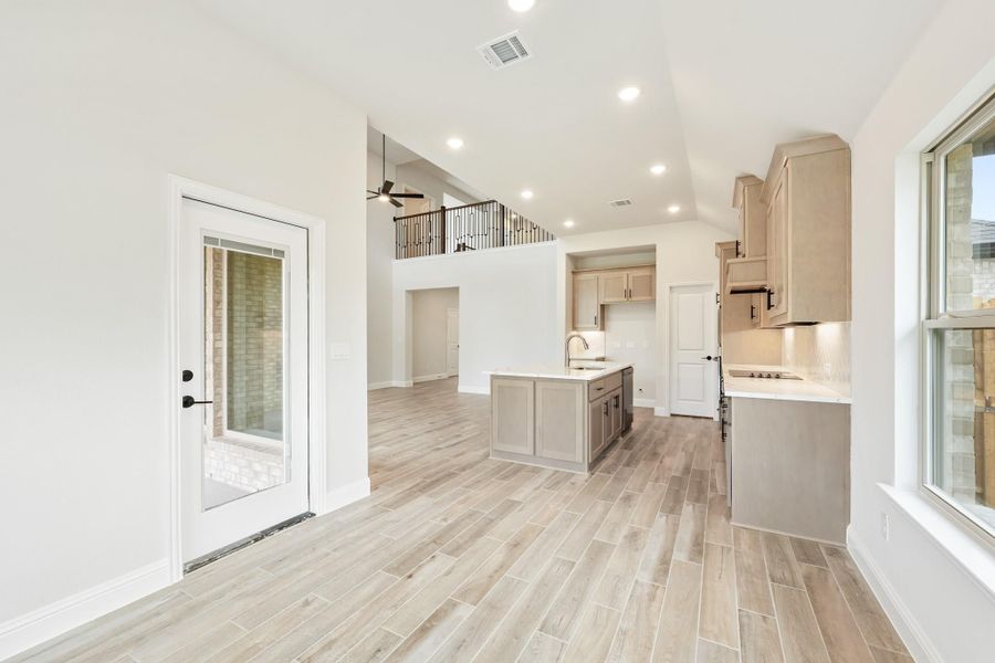 Open-concept kitchen with center island, tan cabinets, light wood-look floors, and second-floor loft visible above.