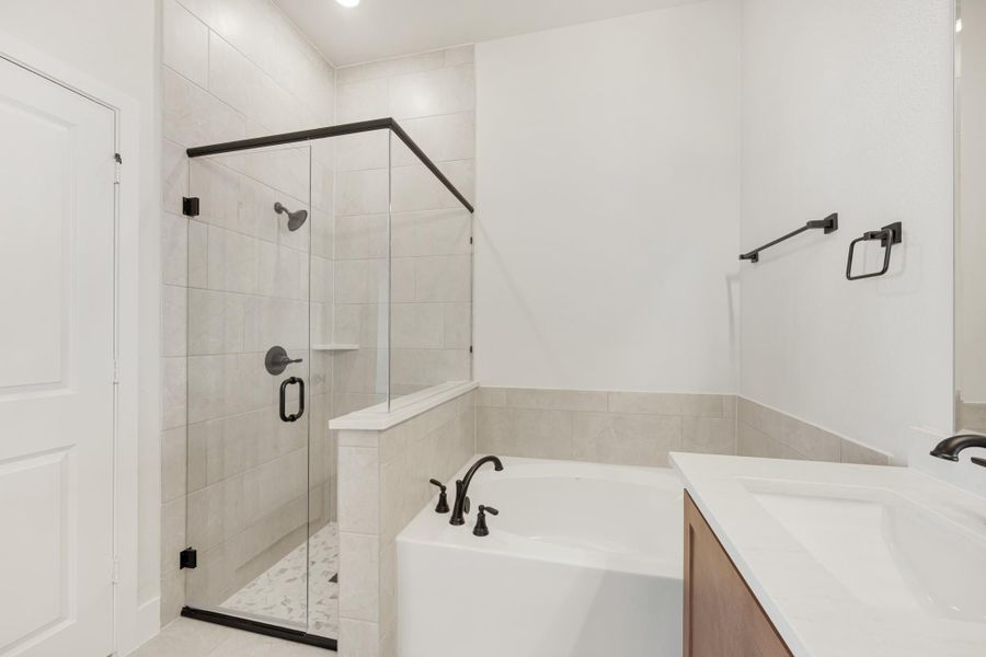 Bathroom with glass-enclosed tile shower, soaking tub, and wood vanity with white countertop