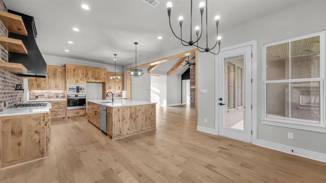 Open-concept kitchen and dining area featuring light wood-finish flooring, a kitchen island with a white countertop and undermount sink, built-in stainless steel appliances, and a brick-patterned backsplash Open-concept kitchen and dining area featuring light wood-finish flooring, a kitchen island with a white countertop and undermount sink, built-in stainless steel appliances, and a brick-patterned backsplash
