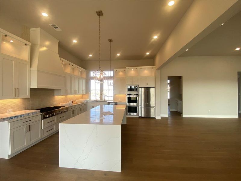 Kitchen featuring decorative light fixtures, appliances with stainless steel finishes, a kitchen island, white cabinets, and tasteful backsplash