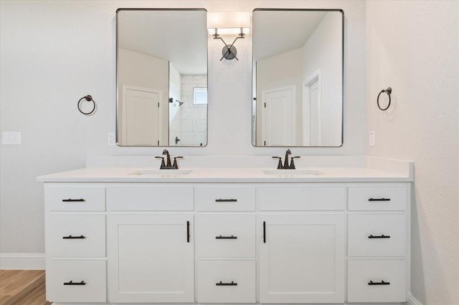 Full bath with a sink, baseboards, double vanity, and tiled shower