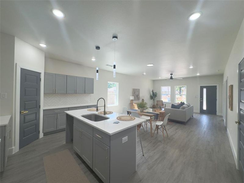 Kitchen with ceiling fan, a center island with sink, dark hardwood / wood-style flooring, hanging light fixtures, and sink