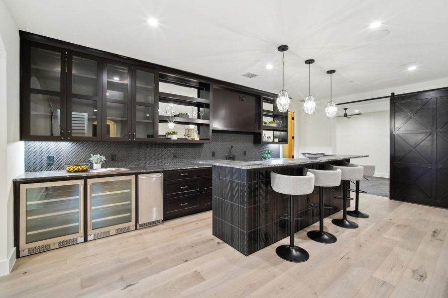 Bar featuring backsplash, a barn door, indoor wet bar, light wood-style flooring, and hanging light fixtures