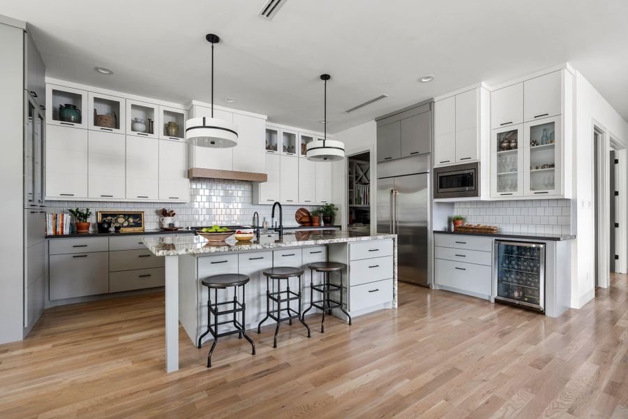 At the center of the kitchen, the oversized waterfall island with diamond arrow granite offers generous prep space and breakfast bar seating, with double pendants overhead and high-end Cafe appliances nearby for everyday ease. The door opens to a huge walk-in pantry with built-ins and matching counters for appliance storage.