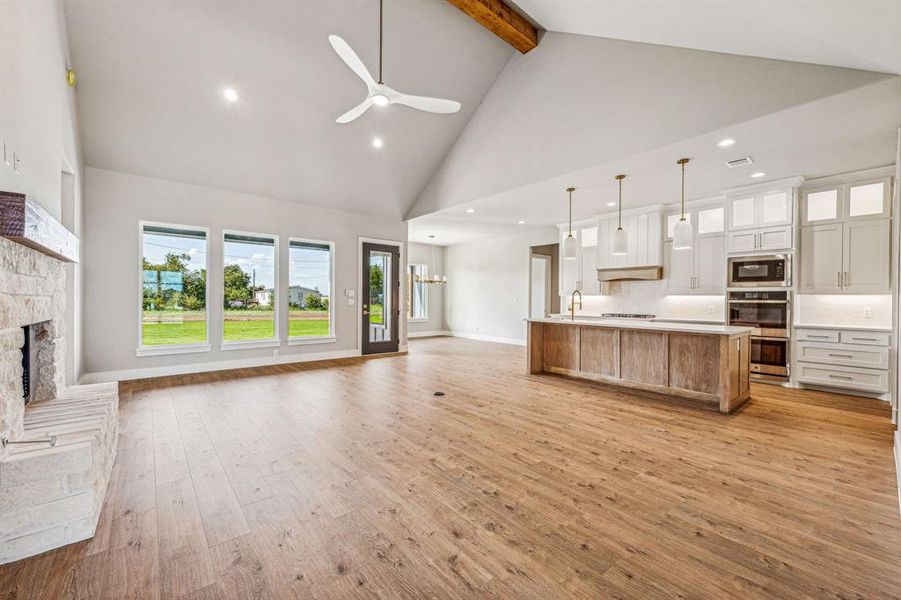 Kitchen featuring a stone fireplace, light hardwood / wood-style floors, decorative light fixtures, and high vaulted ceiling