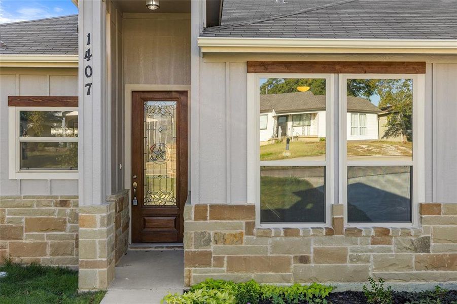 View of exterior entry featuring roof with shingles, stone siding, and board and batten siding
