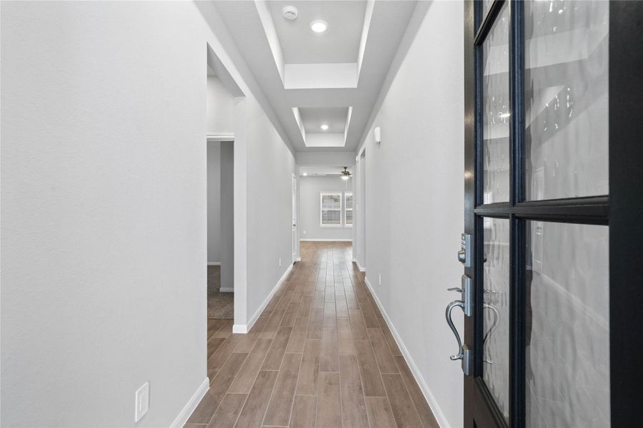 This entryway features a modern, open-concept design. The long, bright corridor utilizes a neutral color palette, recessed lighting, and luxury vinyl flooring to lead the eye toward the home's main living area.