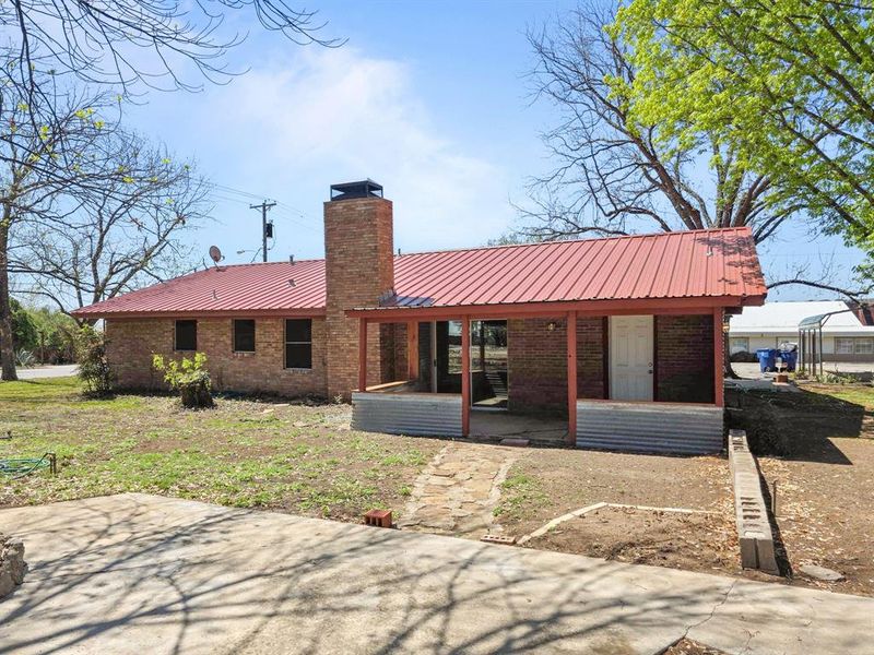 Rear view of house featuring brick siding, metal roof, chimney and covered porch Rear view of house featuring brick siding, metal roof, chimney and covered porch