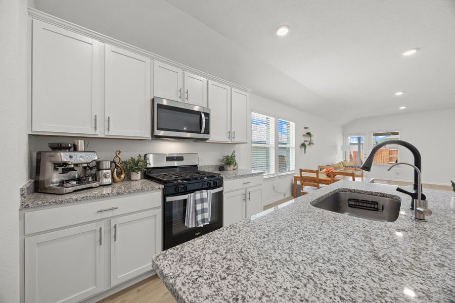 Kitchen with stainless steel appliances, light stone countertops, white cabinetry, recessed lighting, and light wood-style flooring