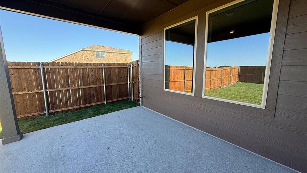 Covered concrete patio with a dark wood privacy fence and established grass