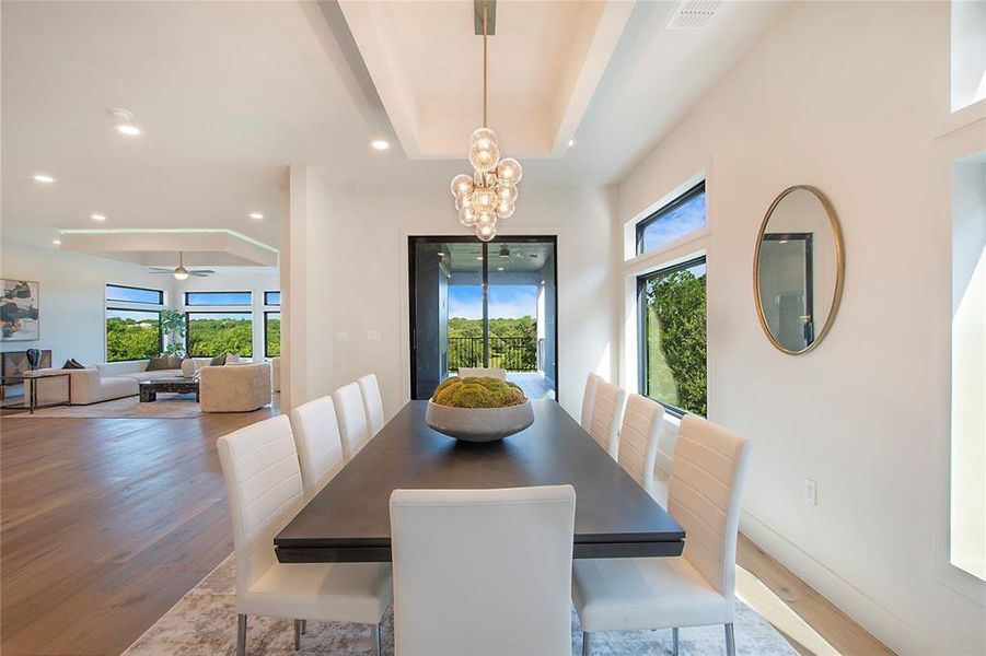 Dining room featuring ceiling fan with notable chandelier, a raised ceiling, light hardwood / wood-style flooring, and a wealth of natural light