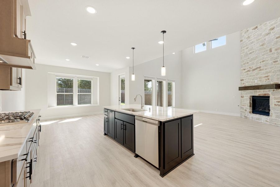 Open-concept kitchen with dark island, quartz countertops, and stone fireplace in adjoining living area