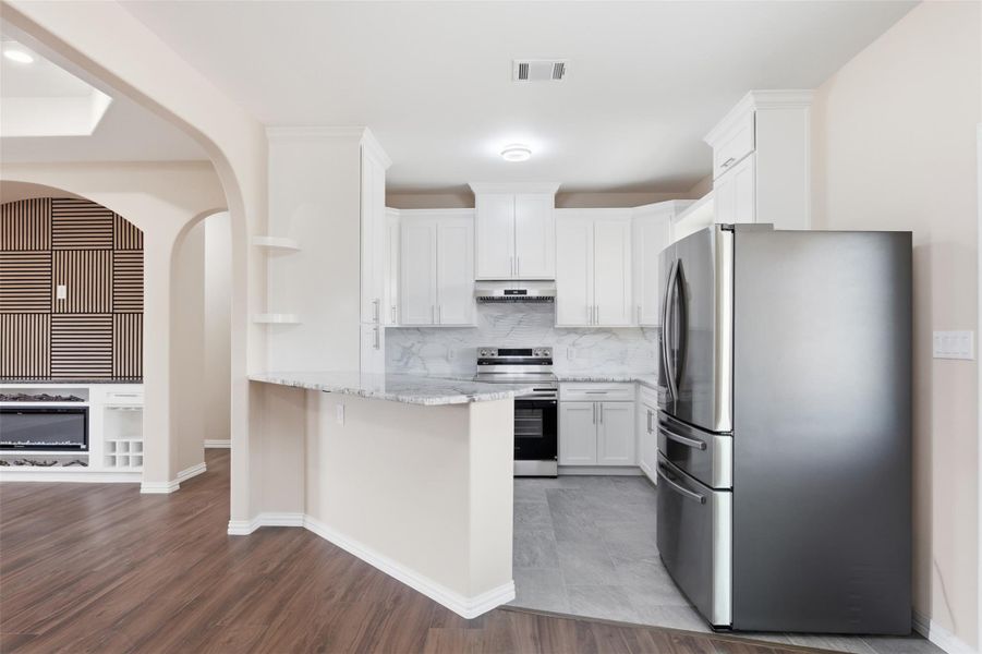 Kitchen featuring stainless steel appliances, white cabinetry, light stone counters, a peninsula, and light wood-style floors