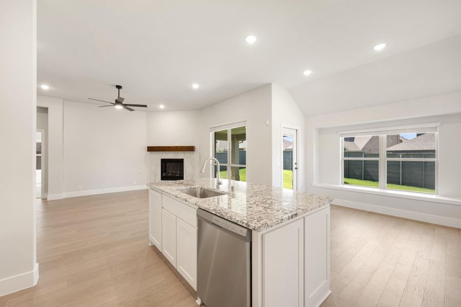 Kitchen island with granite countertop and sink, open to living area with fireplace and light wood floors