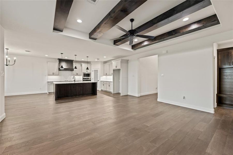 Unfurnished living room featuring beamed ceiling, recessed lighting, light wood-type flooring, ceiling fan, and a chandelier
