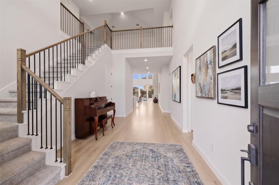 Wide-plank luxury vinyl floors bring warmth and richness to the entry, while a decorative chandelier and soft recessed lighting create an inviting glow. A dedicated closet and discreet storage beneath the wrought iron staircase add thoughtful functionality, keeping the space beautifully organized while maintaining its comfortable, refined feel. This photo has been virtually staged.