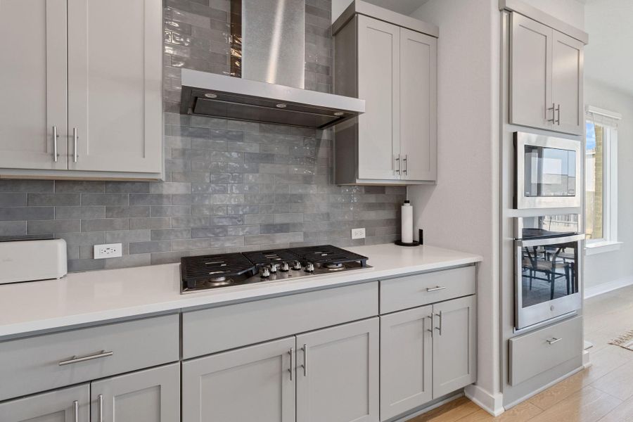 Kitchen with decorative backsplash, gas cooktop, exhaust hood, and stainless steel appliances