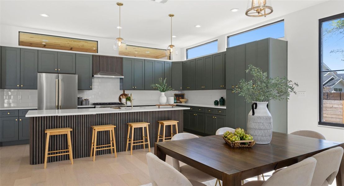 Kitchen featuring decorative light fixtures, high end refrigerator, an island with sink, a breakfast bar, and light wood-style floors