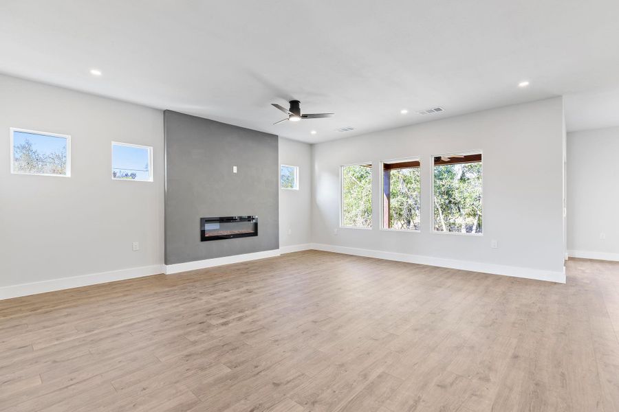 Unfurnished living room with healthy amount of natural light, a large fireplace, light wood-style flooring, recessed lighting, and ceiling fan