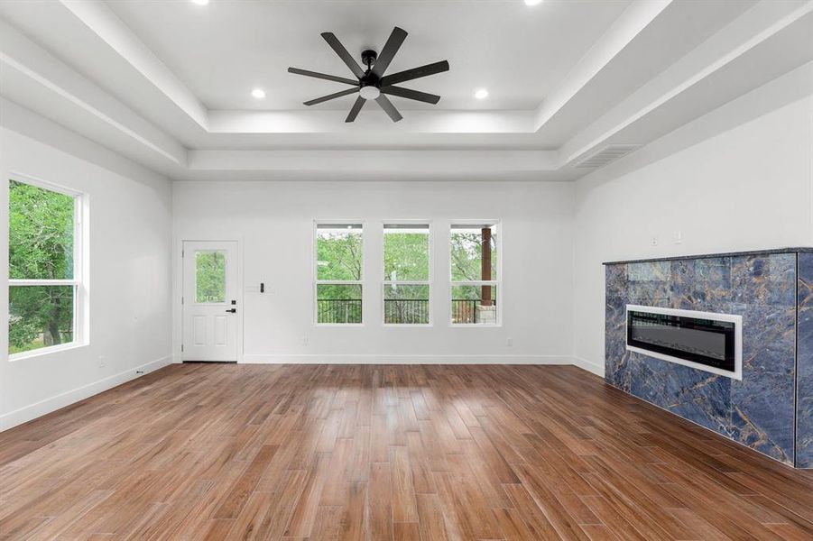 living room with a tray ceiling, plenty of natural light, wood finished floors, and a premium fireplace