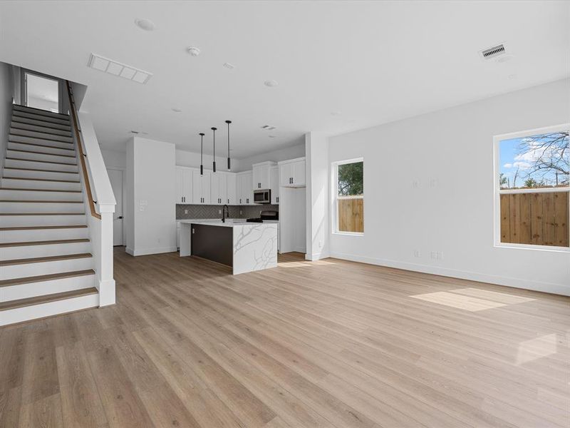 This modern kitchen features sleek white cabinetry, stainless steel appliances, and a stylish island with seating for three. The open layout is enhanced by pendant lighting and a large window that brings in natural light, creating a bright and inviting space.