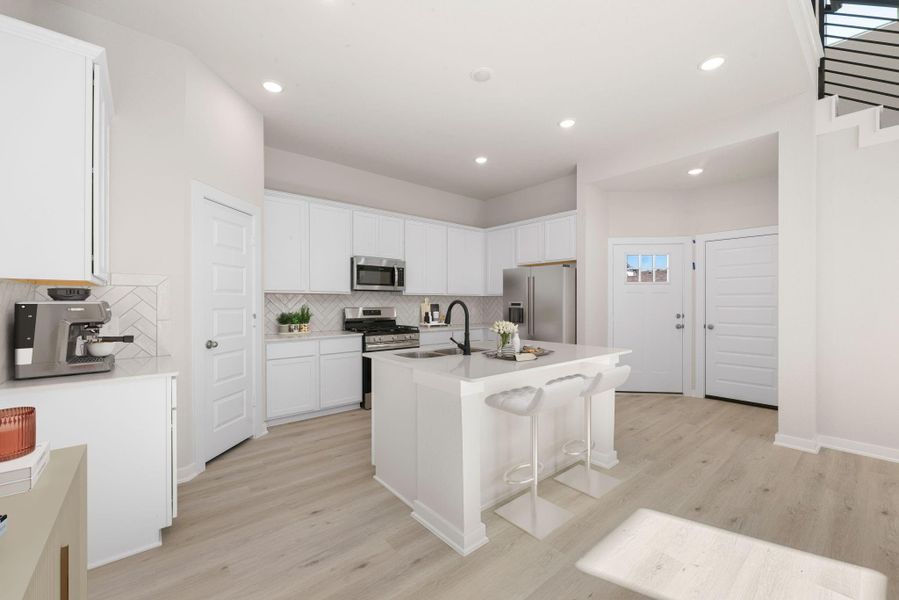 This elegant kitchen showcases crisp white cabinetry, stainless steel appliances, and a stylish herringbone backsplash. The large center island with bar seating offers the perfect spot for casual dining or entertaining, while the open layout enhances the home’s bright and inviting atmosphere.