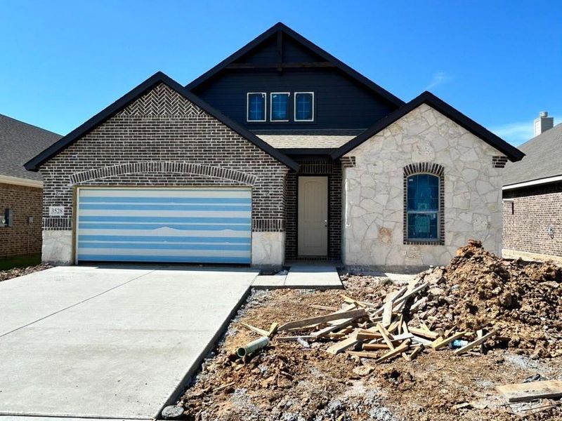 View of front facade featuring concrete driveway, a garage, brick siding, and stone siding