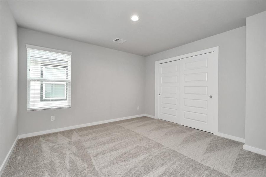 Secondary bedroom with neutral paint, plush carpet, and large windows for natural light.