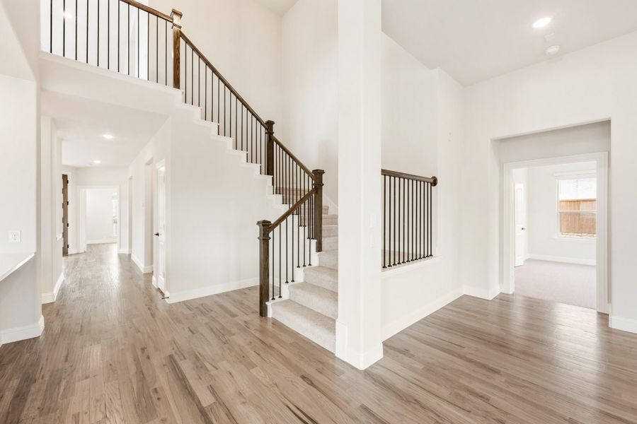 Open foyer with two-story staircase, dark wood railings, and light hardwood floors