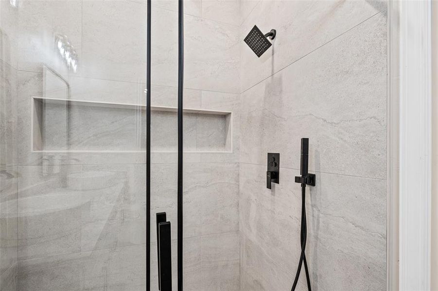Walk-in shower featuring light-toned tile, a matte black rain shower head, a handheld shower fixture, and a built-in shower niche