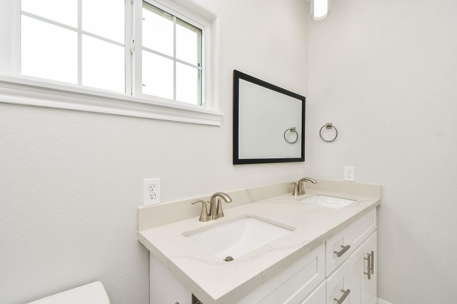 This photo showcases a modern bathroom with a double sink vanity, sleek marble countertops, brushed nickel faucets, and a large framed mirror. The space is bright and airy, enhanced by a window allowing natural light.