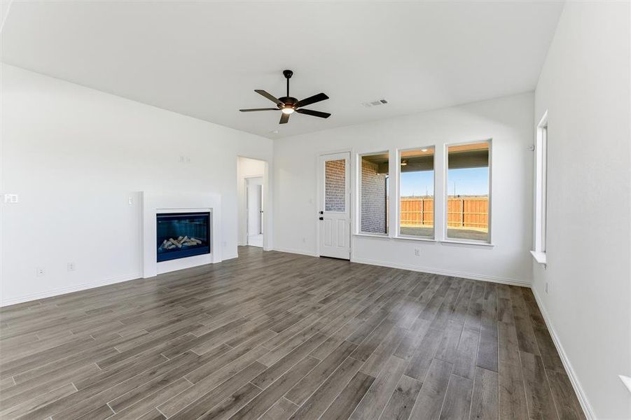 Unfurnished living room with a glass covered fireplace, wood finished floors, and a ceiling fan