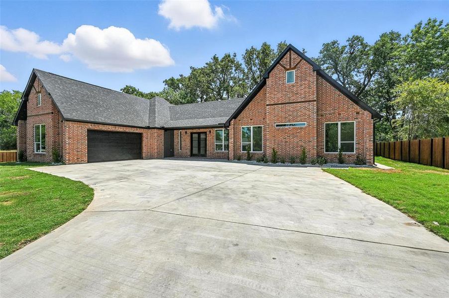 Tudor house with brick siding, an attached garage, a shingled roof, and concrete driveway Tudor house with brick siding, an attached garage, a shingled roof, and concrete driveway