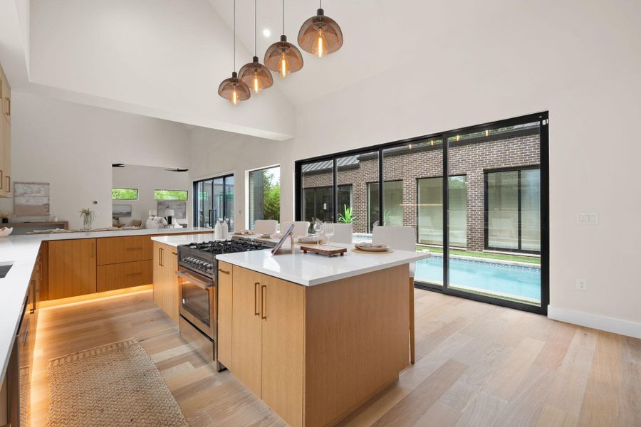 Vaulted ceiling kitchen featuring a large island with built-in range, wood-finish cabinetry, white countertops, and wood-finish flooring