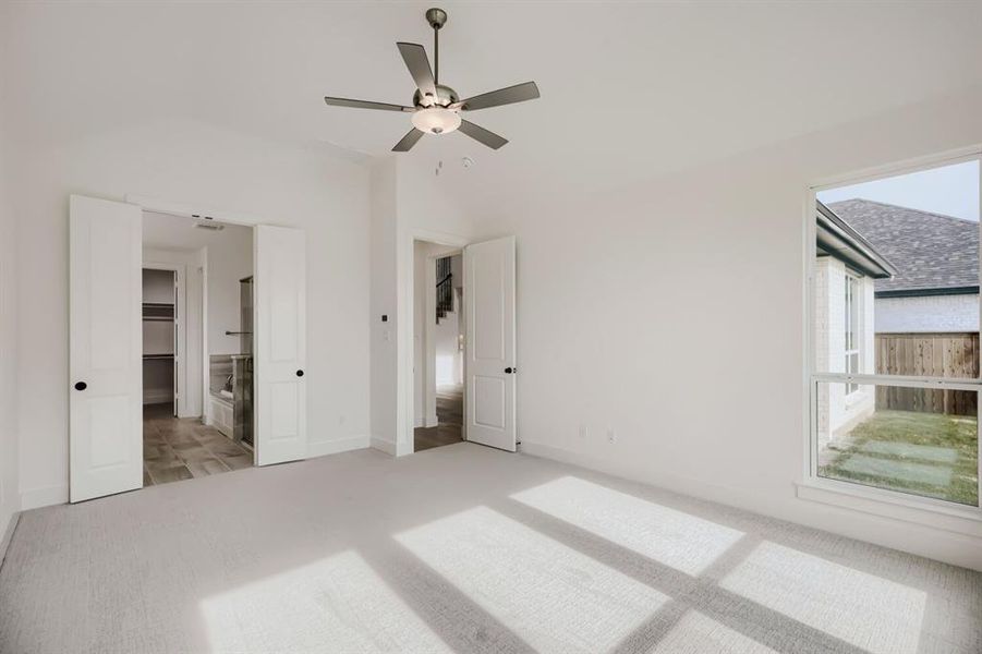 Unfurnished bedroom with ensuite bath, light carpet, a ceiling fan, and lofted ceiling