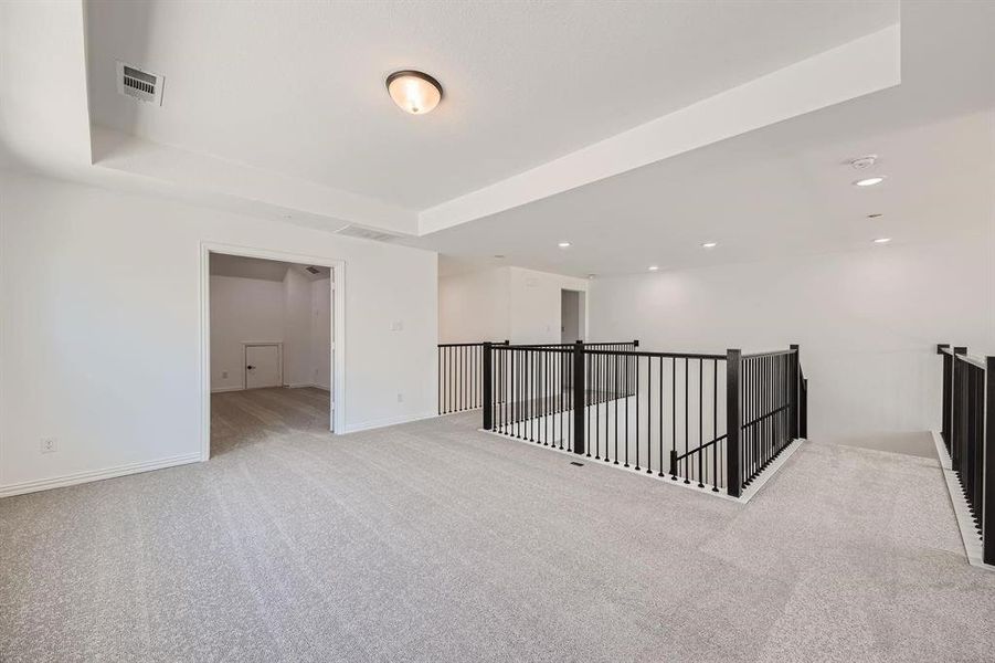 Expansive carpeted loft area featuring a tray ceiling, recessed lighting, and modern black balusters Expansive carpeted loft area featuring a tray ceiling, recessed lighting, and modern black balusters