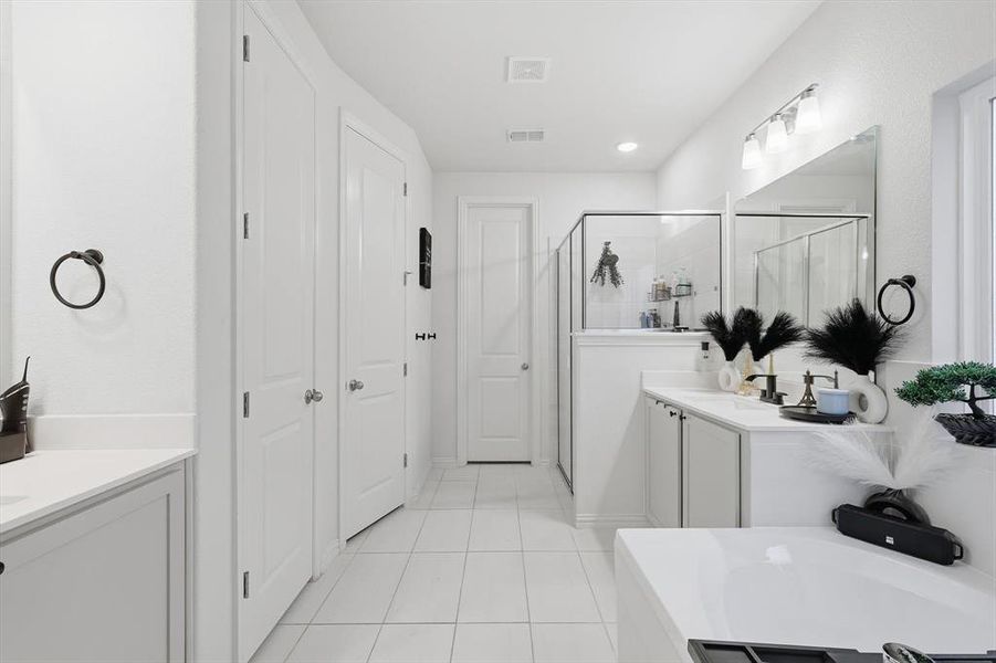 Bathroom featuring a bath, two vanities, a stall shower, light tile patterned flooring, and a closet