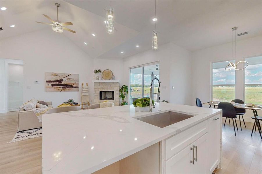 Kitchen featuring ceiling fan with notable chandelier, light stone countertops, a wealth of natural light, and a fireplace