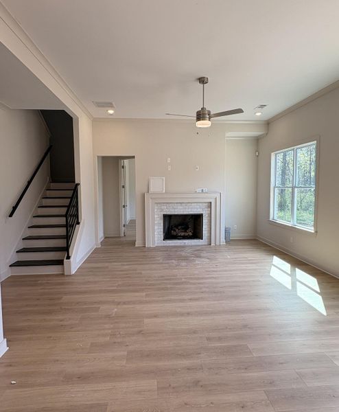 Unfurnished living room featuring a tiled fireplace, light wood-style flooring, a ceiling fan, and crown molding